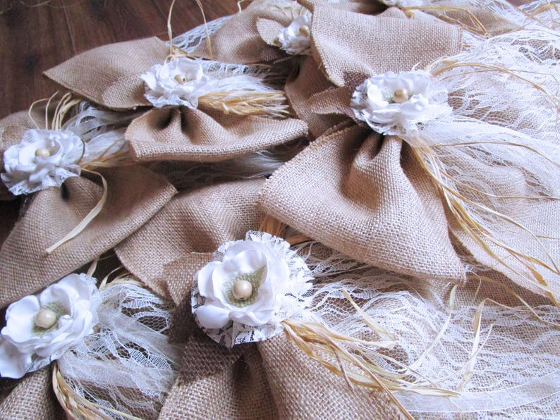 May include: A collection of burlap bows with white lace and a white flower accent. The bows are tied with twine and have wheat stalks attached.