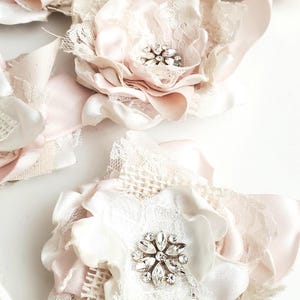 small fabric flowers made with bits of burlap, cotton, and lace. the center is accented by rhinestone small buttons. blush and ivory colors