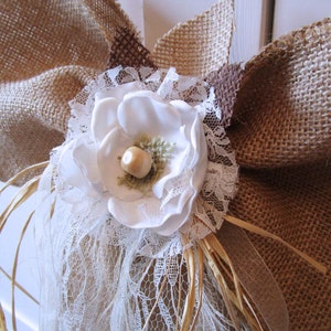 May include: A white fabric flower with a brown center, surrounded by white lace and burlap fabric.