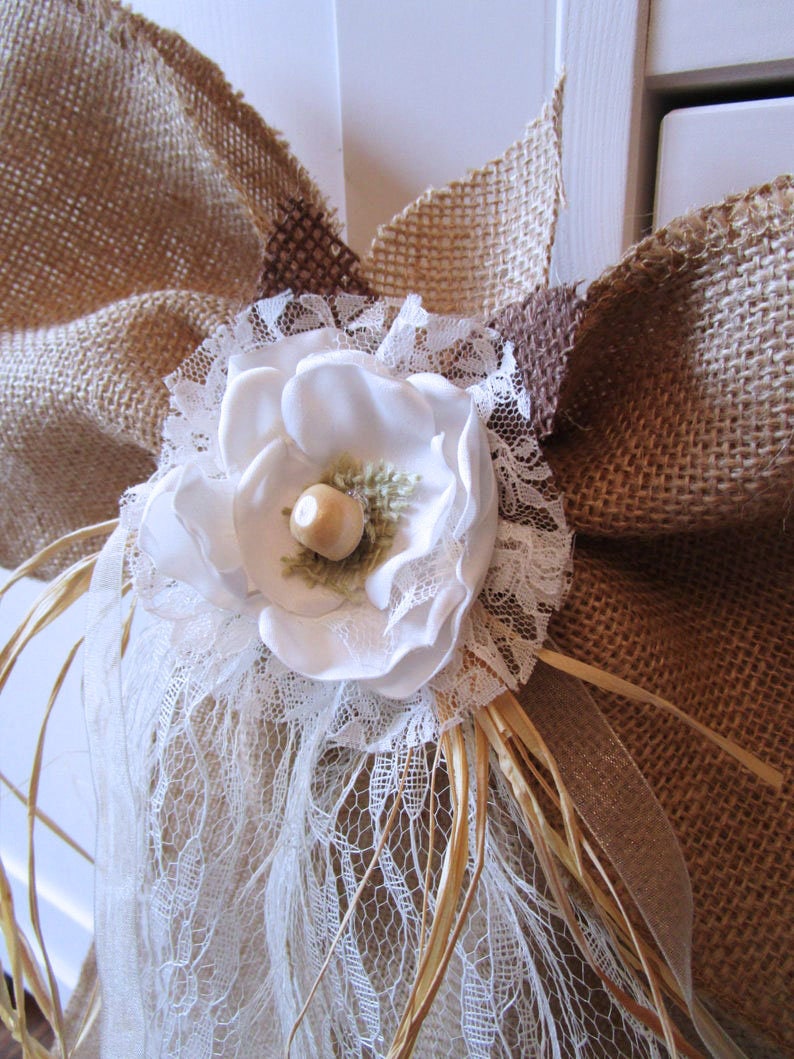 May include: A white fabric flower with a brown center, surrounded by white lace and burlap fabric.