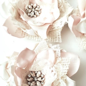 small fabric flowers made with bits of burlap, cotton, and lace. the center is accented by rhinestone small buttons. blush and ivory colors