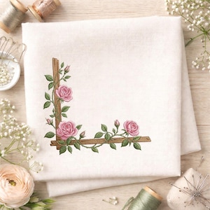May include: A white linen cloth with an embroidered design of pink roses and green leaves climbing a brown wooden trellis. The floral design is in the corner of the cloth.