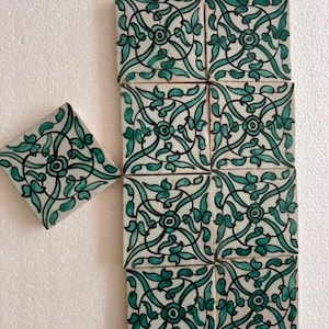 May include: A collection of square ceramic tiles featuring a repeating teal and black floral vine pattern on a white background. The tiles are arranged in a grid, with one tile positioned separately to the left of the main rectangular block.
