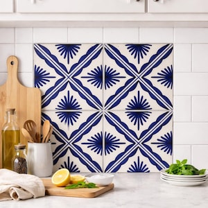 Peut inclure: Quatre carreaux carrés avec un motif géométrique bleu et blanc répétitif. Le motif présente une forme centrale en éventail avec des lignes rayonnantes, encadrée par une double bordure bleue. Les carreaux sont posés sur un dosseret carrelé blanc.