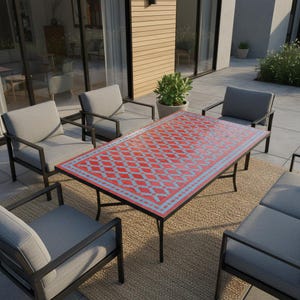 May include: Outdoor patio furniture set featuring a rectangular table with a red and blue patterned top, surrounded by gray cushioned chairs with black metal frames. The table is approximately 60 inches long. The set is on a woven rug.