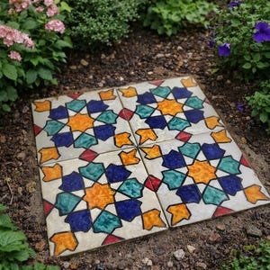 May include: Four square ceramic tiles with a colorful starburst pattern in a garden setting. The design features orange, blue, teal, and red geometric shapes on a cream background. The tiles are surrounded by soil and greenery.