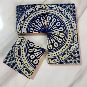 Peut inclure: Trois carreaux de céramique carrés présentant une base blanche avec des motifs complexes peints à la main en bleu foncé. Chaque carreau affiche un motif circulaire partiel avec des lignes rayonnantes, des points et des formes florales.