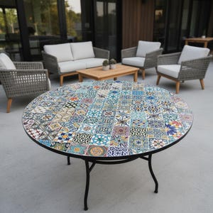 May include: A round outdoor table with a mosaic tile top featuring a variety of colorful patterns. The table has a black metal frame and legs. The table is surrounded by outdoor furniture.