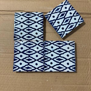 Peut inclure: Trois carreaux de céramique carrés présentant un motif géométrique répétitif bleu foncé et blanc. Le design se compose de formes en losange interconnectées avec un petit point bleu plein centré dans chaque losange, créant une grille uniforme.