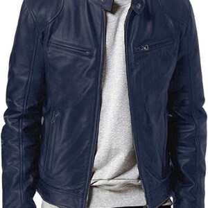 Peut inclure: Une veste en cuir bleu marine dotée d'un col montant avec fermeture à bouton-pression, d'une fermeture éclair frontale intégrale et de deux poches poitrine horizontales zippées. La veste est portée sur un t-shirt gris clair et un pantalon noir.
