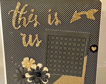 May include: A square photo frame with a black and white polka dot design. The words "this is us" are in gold glitter lettering. A gold glitter arrow and a black heart button are on the frame. The frame has a black and grey patterned photo area and decorative flowers.