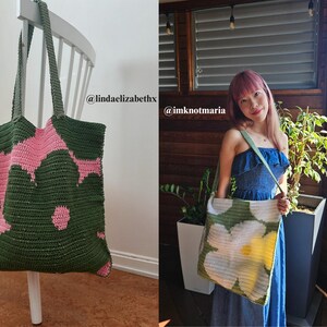 Puede incluir: Un bolso tote grande, hecho a mano, con un estampado floral verde y rosa. El bolso est&aacute; hecho de un material de ganchillo y tiene asas largas. El bolso se muestra colgado de una silla blanca.