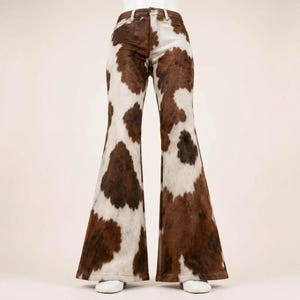 May include: High-waisted flared pants featuring a brown and white cow print pattern. The garment has a classic five-pocket design with a button and zipper fly closure, fitted through the hips and thighs, and wide, dramatic flared leg openings.