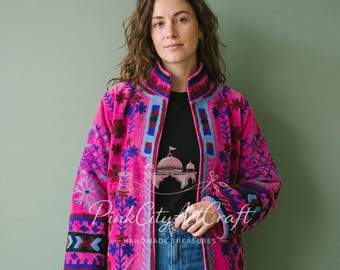 May include: A vibrant pink jacket featuring intricate multi-colored floral and geometric embroidery, a high collar, and long sleeves. The garment displays a central logo with the text Pink City Craft Handmade Treasures in white script.