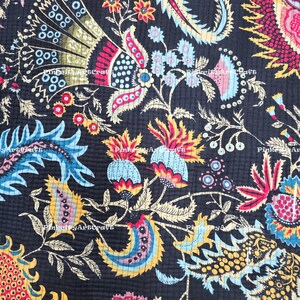 Può includere: Primo piano di un tessuto scuro con un vivace motivo floreale. Il design presenta grandi fiori e foglie stilizzate nei toni del rosso, blu, giallo e bianco su uno sfondo nero. Il tessuto ha una trama trapuntata.