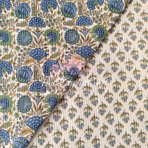 May include: A quilted fabric featuring a large-scale floral pattern in blue, green, and tan on an off-white background, layered over a smaller floral print. The text PureCityArtCraft is visible in the center of the folded textile material.