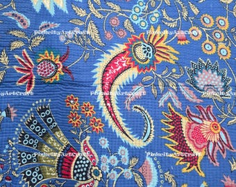 Könnte beinhalten: Nahaufnahme eines blauen Stoffes mit detailliertem Blumenmuster. Das Design zeigt große Paisley-Formen in Rot, Gelb und Weiß, zusammen mit kleineren Blumen und Blättern. Der Stoff hat eine gesteppte Textur.