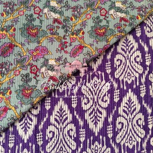 May include: A quilted fabric featuring two distinct patterns. The top section displays a light green background with a floral print in pink, yellow, and dark green. The bottom section shows a purple and white ikat-style geometric pattern.