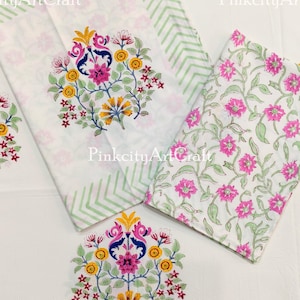 Puede incluir: Tela blanca con estampados florales. Una pieza presenta un gran diseño floral central en rosa, amarillo y azul. Otra tiene un estampado floral rosa sobre fondo blanco. Una tercera pieza tiene un borde verde en zigzag.