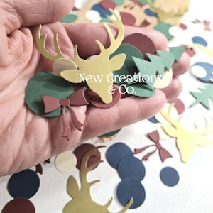 May include: A collection of paper cutouts in various shapes and colors, including gold deer heads, green circles, burgundy bows, and blue circles. The text "New Creations & Co." is visible. These festive elements are suitable for crafting or holiday decorations.