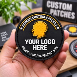 Puede incluir: Un parche circular de PVC negro con una silueta amarilla de una cabeza humana en el centro. El texto dice HUMAN CUSTOM PATCHES en la parte superior, YOUR LOGO HERE en el medio y ORDER YOUR PVC PATCHES NOW en el borde inferior.