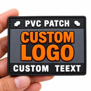 May include: A rectangular PVC patch with a black border and a dark grey centre. The top section features the white text PVC PATCH with small white icons. The centre displays the bold orange text CUSTOM LOGO. The bottom section shows white text CUSTOM TEEXT.