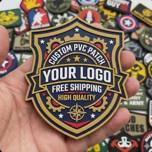 Könnte beinhalten: Ein marineblaues und goldenes PVC-Patch mit dem Text "CUSTOM PVC PATCH" und "YOUR LOGO". Das Patch hat eine Schildform mit einem Kompassrosen-Design und den Worten "FREE SHIPPING" und "HIGH QUALITY".