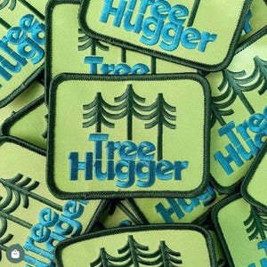 Może przedstawiać: Kolekcja kwadratowych naszywek z jasnozielonym tłem i ciemnozieloną obwódką. Każda naszywka zawiera wzór trzech stylizowanych drzew i słowa "Tree Hugger" w kolorze niebieskim.