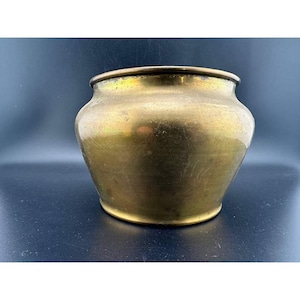 May include: A vintage brass pot with a rounded body and a slightly flared rim. The pot has a tarnished, aged appearance, with variations in the golden color. The pot is likely used for decorative purposes or as a planter.