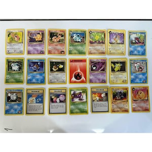 May include: A collection of twenty-one rectangular trading cards arranged in three rows of seven. The cards feature various colorful illustrations of creatures, energy symbols, and trainer characters with printed text, borders, and game statistics.
