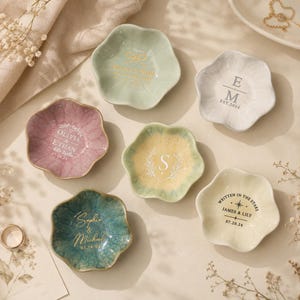 May include: Six flower-shaped ceramic trinket dishes in various colors including sage green, dusty rose, yellow, teal, and white. Each dish features custom text and graphics, such as names, dates, and monograms, printed in gold, white, or black ink.