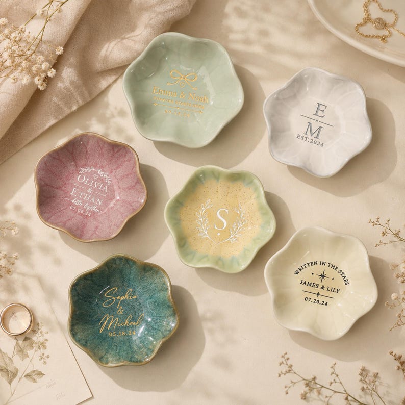 May include: Six flower-shaped ceramic trinket dishes in various colors including sage green, dusty rose, yellow, teal, and white. Each dish features custom text and graphics, such as names, dates, and monograms, printed in gold, white, or black ink.