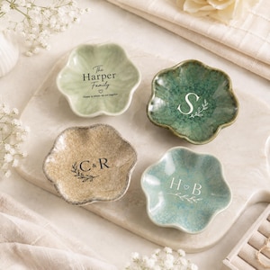 May include: Four flower-shaped ceramic trinket dishes in light green, dark green, beige, and blue. Each dish features custom text: The Harper Family, S, C & R, and H & B, accompanied by small heart and leaf illustrations printed in white or black.
