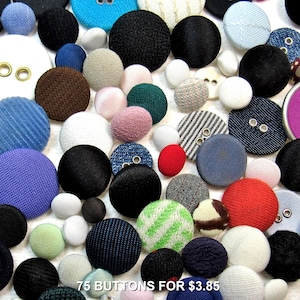 May include: A collection of 75 fabric-covered buttons in various sizes, colors, and textures, including solid black, white, blue, red, and green, as well as striped and patterned designs, with some featuring metal eyelets and the text 75 BUTTONS FOR $3.85.