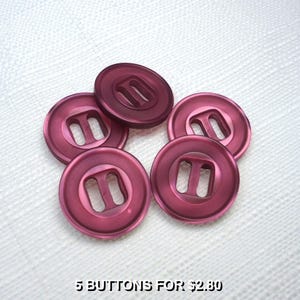 May include: Five round, plum-colored buttons with a rectangular opening in the center. The buttons are arranged in a circular pattern on a white textured surface. The text "5 BUTTONS FOR $2.80" is at the bottom.