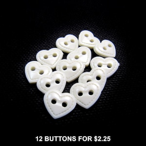 Może przedstawiać: Dwunastka kremowych guzików w kształcie serca, każdy z dwoma otworami, na czarnym tle. Na dole obrazu widnieje napis "12 BUTTONS FOR $2.25".