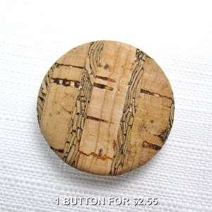 May include: A round, natural cork button with a textured surface and a light brown color. The button has dark brown and gold-colored linear patterns. The text "1 BUTTON FOR $2.55" is at the bottom of the image.