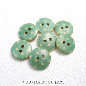 May include: Seven round, light green wooden buttons, each featuring two central holes and a pattern of small, pale yellow polka dots. The buttons are arranged in a cluster, displaying a smooth, circular shape with a visible wood grain texture.