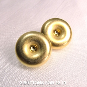 May include: Two circular gold-toned buttons with a smooth, matte finish and a raised, polished center point. The buttons have a concave, donut-like shape with a rounded outer edge. The text 2 BUTTONS FOR $2.10 is visible at the bottom.