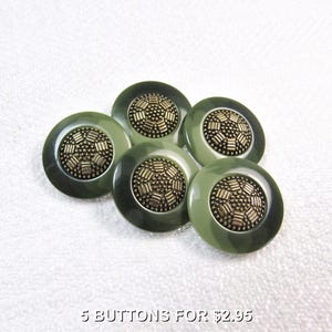 May include: Five round olive green buttons, each featuring a central metallic bronze-toned inlay with a textured, geometric pattern of small raised dots and rectangular bars arranged in a circular design, set against a smooth, solid-colored rim.