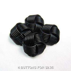 May include: Four black buttons, each featuring a spherical shape constructed from a continuous, coiled cord design. The buttons have a glossy finish and a complex, interwoven pattern that creates a textured, rounded appearance on all sides.