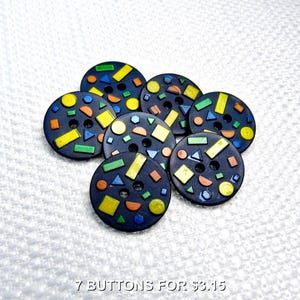 May include: Seven navy blue buttons with colorful geometric shapes in yellow, orange, green, and blue. The buttons are round with two holes for sewing. The shapes include rectangles, triangles, and circles.