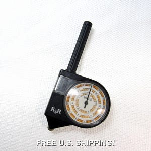 May include: Black and clear K&R miles measuring tool. The tool has a black handle and a circular dial with white and orange markings. The dial reads "MILES".