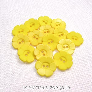 May include: A collection of fifteen yellow flower-shaped buttons. Each button has a two-hole design in the center. The buttons are arranged on a white textured surface.