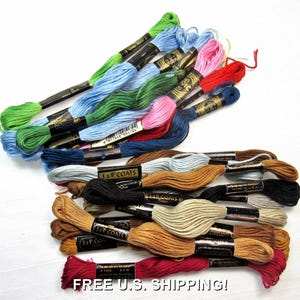 Könnte beinhalten: Eine Sammlung von Stickgarnen in verschiedenen Farben, darunter Grün, Blau, Rosa und Braun. Das Garn ist gebündelt und mit Markeninformationen versehen. Das Bild zeigt eine Vielzahl von Farben, ideal für Bastel- und Stickprojekte.