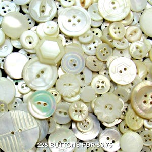 May include: A large collection of assorted white and cream-colored buttons in various shapes, sizes, and designs, including round, hexagonal, and scalloped edges, with two or four holes, featuring the text 225 BUTTONS FOR $3.75.