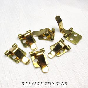 May include: Six brass-colored clasps are arranged on a white surface. Each clasp has a rectangular base with a curved, hinged top. The clasps are designed to secure items. The text at the bottom reads "6 CLASPS FOR $3.95".