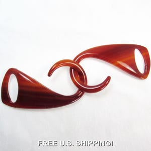 May include: A brown, interlocking clasp with a polished finish. The clasp has two curved, elongated pieces with oval openings, connected by a circular link. The color is a rich, warm brown with lighter streaks, creating a marbled effect. The text "FREE U.S. SHIPPING!" is at the bottom.