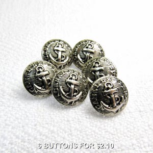 Puede incluir: Seis botones de metal plateados con un diseño de ancla. Cada botón tiene un ancla en relieve y las palabras "Made in China" alrededor del borde.