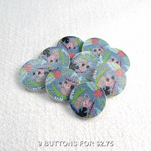 May include: A collection of nine round buttons featuring a blue base with a multi-colored botanical print. Each button has two central holes and displays a pattern of pink, green, and black abstract leaf and floral shapes across the surface.